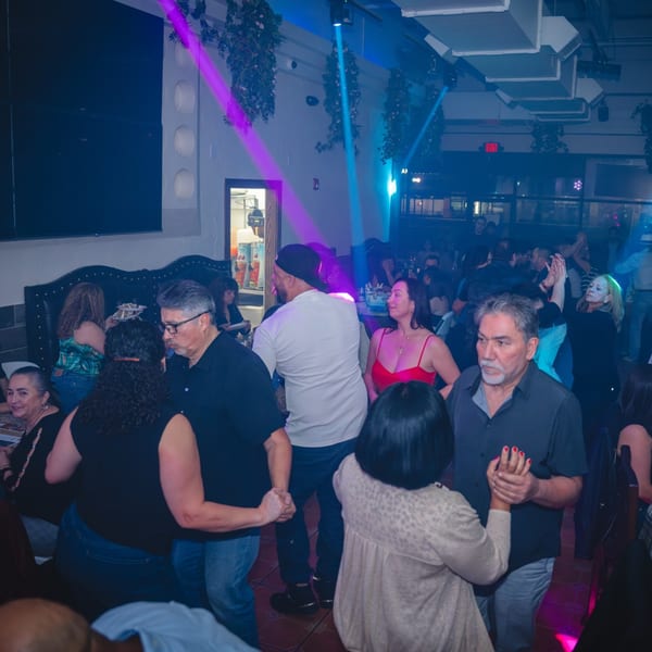 People dancing and socializing in a dimly lit San Jose Mexican Restaurant with purple and blue lights.