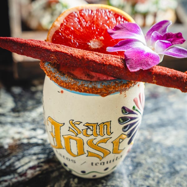 San Jose Mexican Restaurant's drink in a branded mug, garnished with grapefruit, orchid, and chili candy.