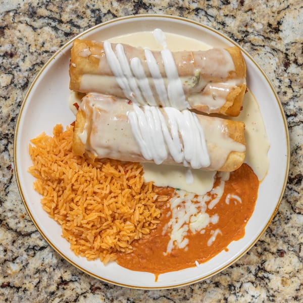 Two chimichangas topped with white sauce and sour cream, served with rice and refried beans.