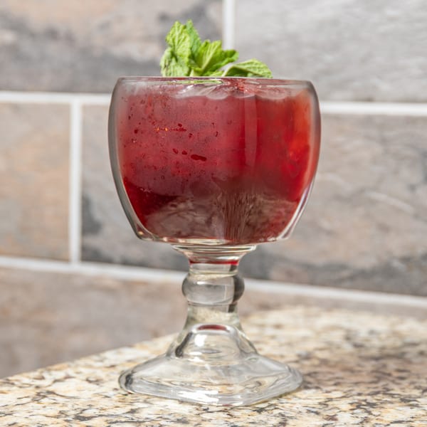 A vibrant red Mexican drink in a goblet, garnished with fresh mint, on a granite countertop.