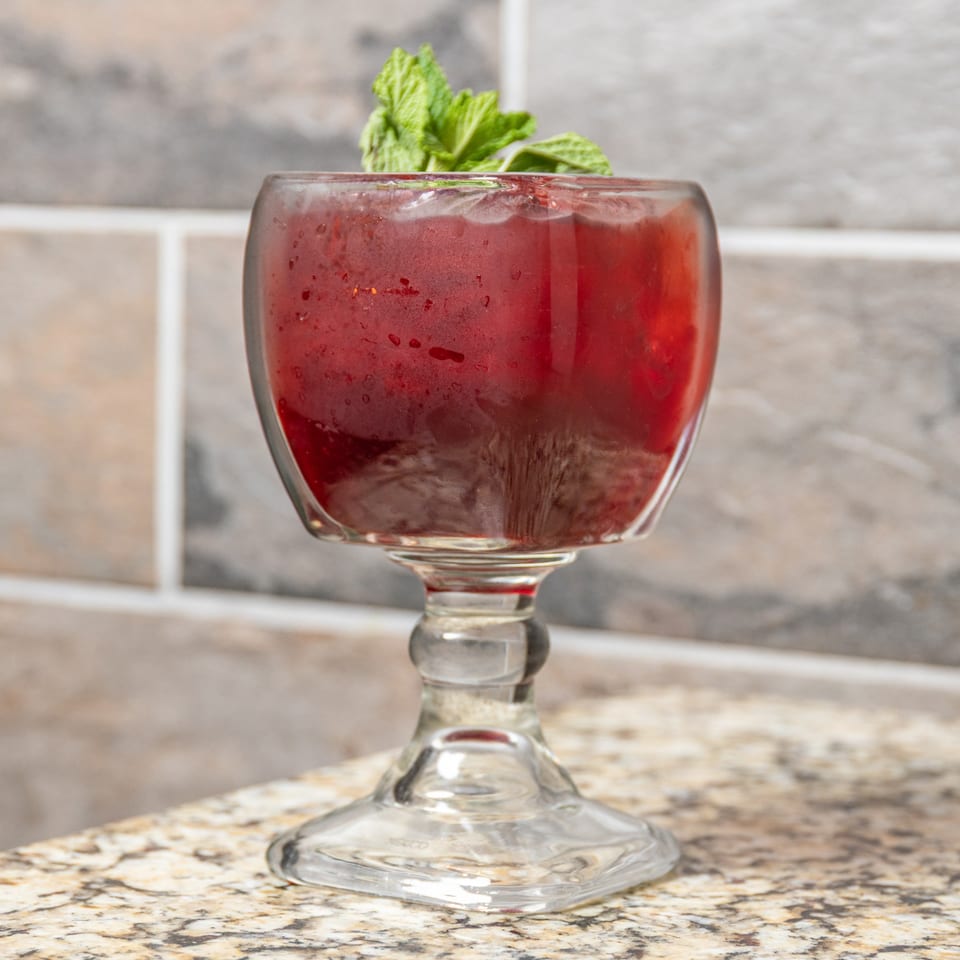 A vibrant red Mexican drink in a goblet, garnished with fresh mint, on a granite countertop.