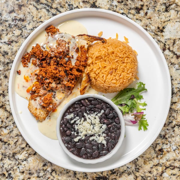 Mexican dish with chicken, chorizo, cheese sauce, rice, black beans, and a small salad.