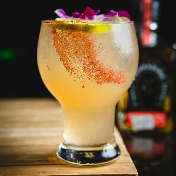San Jose Mexican Restaurant's margarita with chili salt rim, lime, and purple orchid garnish on a wooden table.