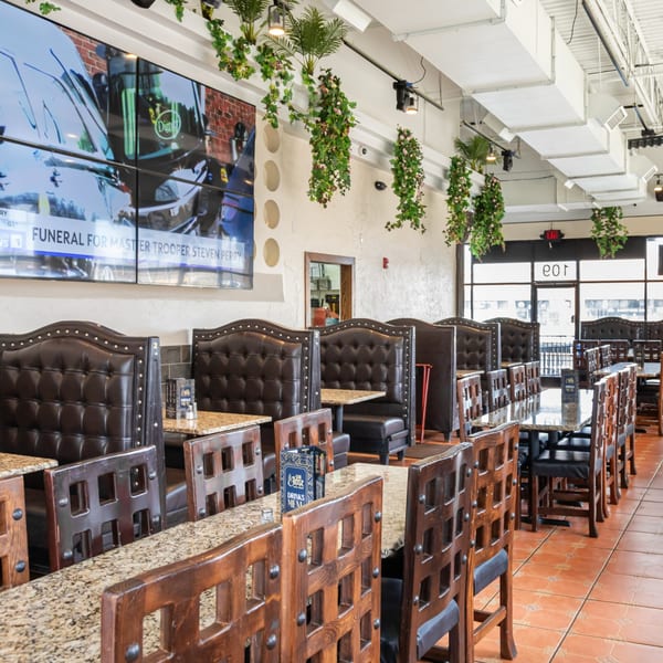 Interior of San Jose Mexican Restaurant with brown leather booths, wooden chairs, granite tables, and hanging plants.
