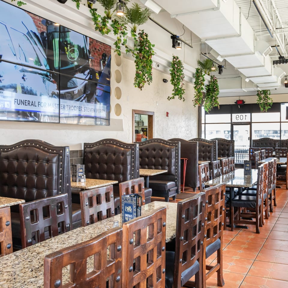 Interior of San Jose Mexican Restaurant with brown leather booths, wooden chairs, granite tables, and hanging plants.