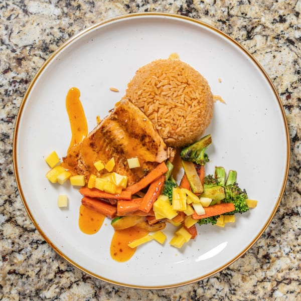 Grilled salmon with mango salsa, rice, and mixed vegetables on a white plate.
