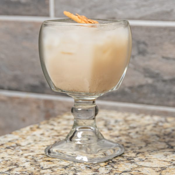 Horchata in a glass goblet with a cinnamon stick, on a granite countertop.