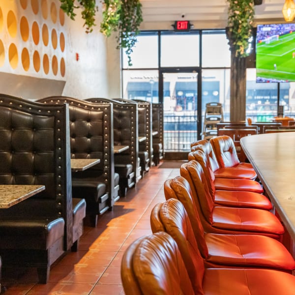 Interior of San Jose Mexican Restaurant with black booths, orange bar stools, and a TV showing soccer.