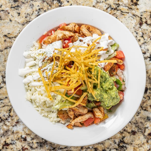 Overhead view of a Mexican chicken bowl with guacamole, sour cream, and tortilla strips.